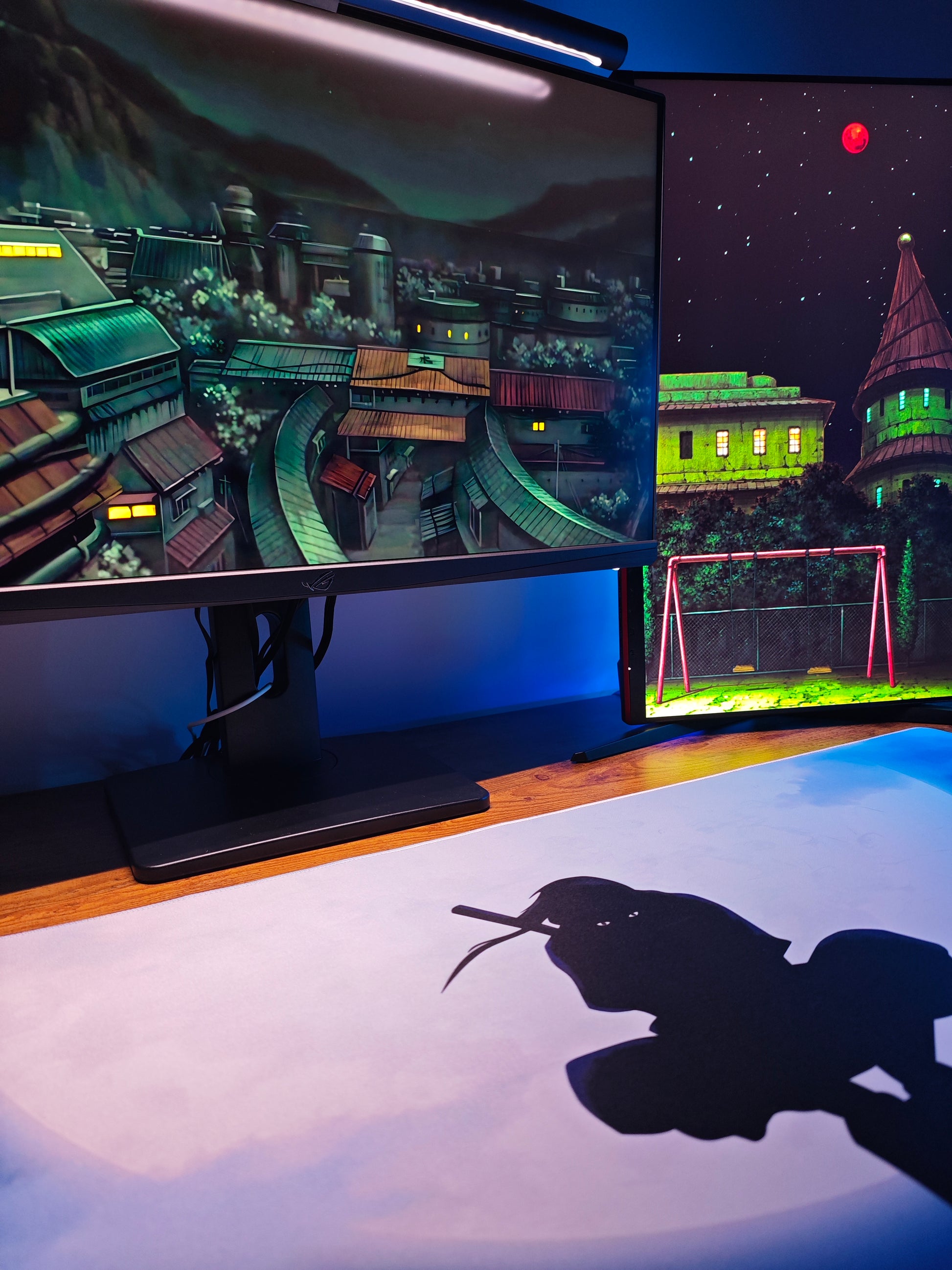 Mousepad Naruto cu personajul Itachi de mari dimensiuni privit pe boirou de gaming cu setup de 2 monitoare.