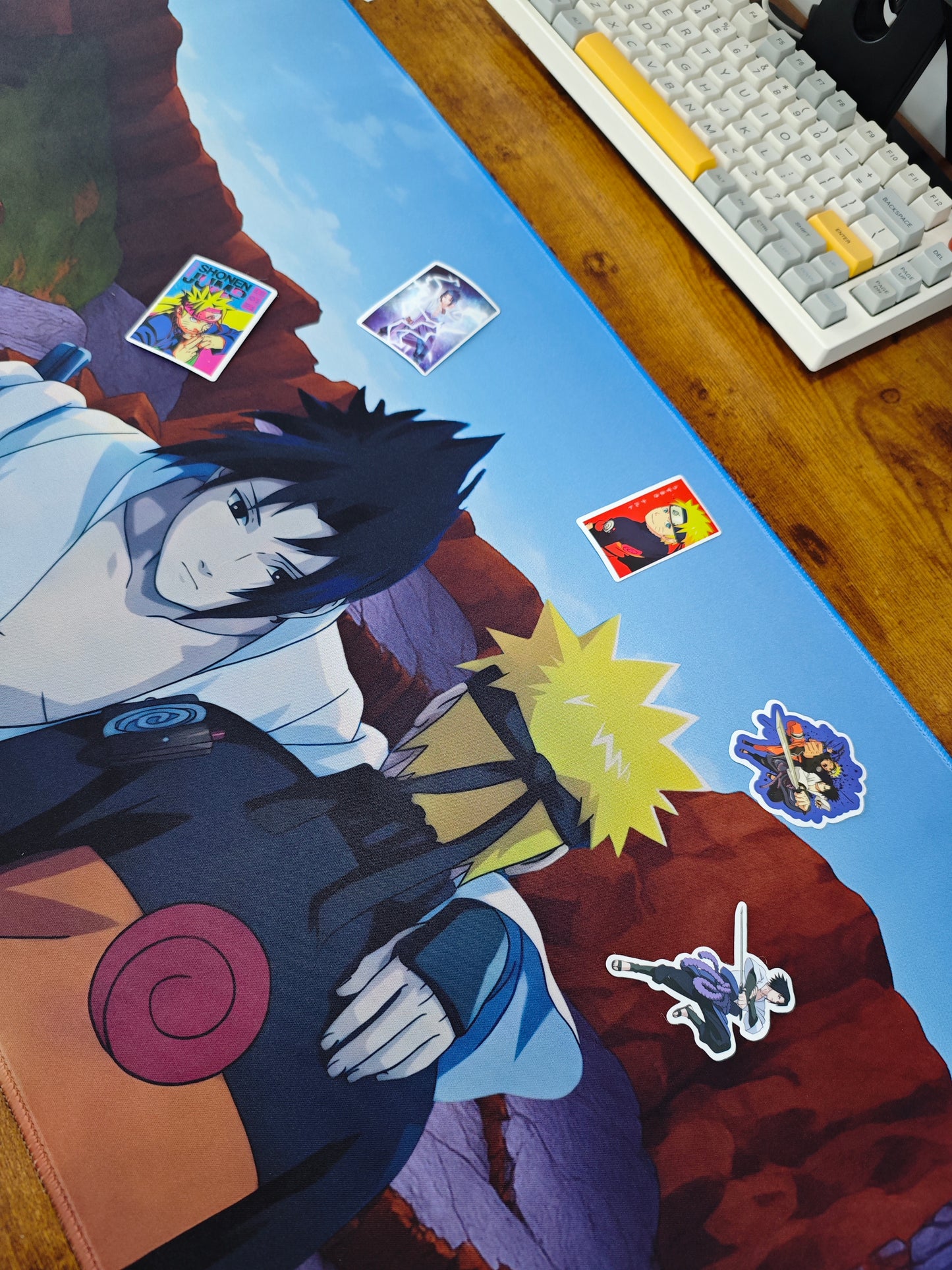 Mousepad Naruto și Sasuke pe un birou de gaming cu stickere lângă.
