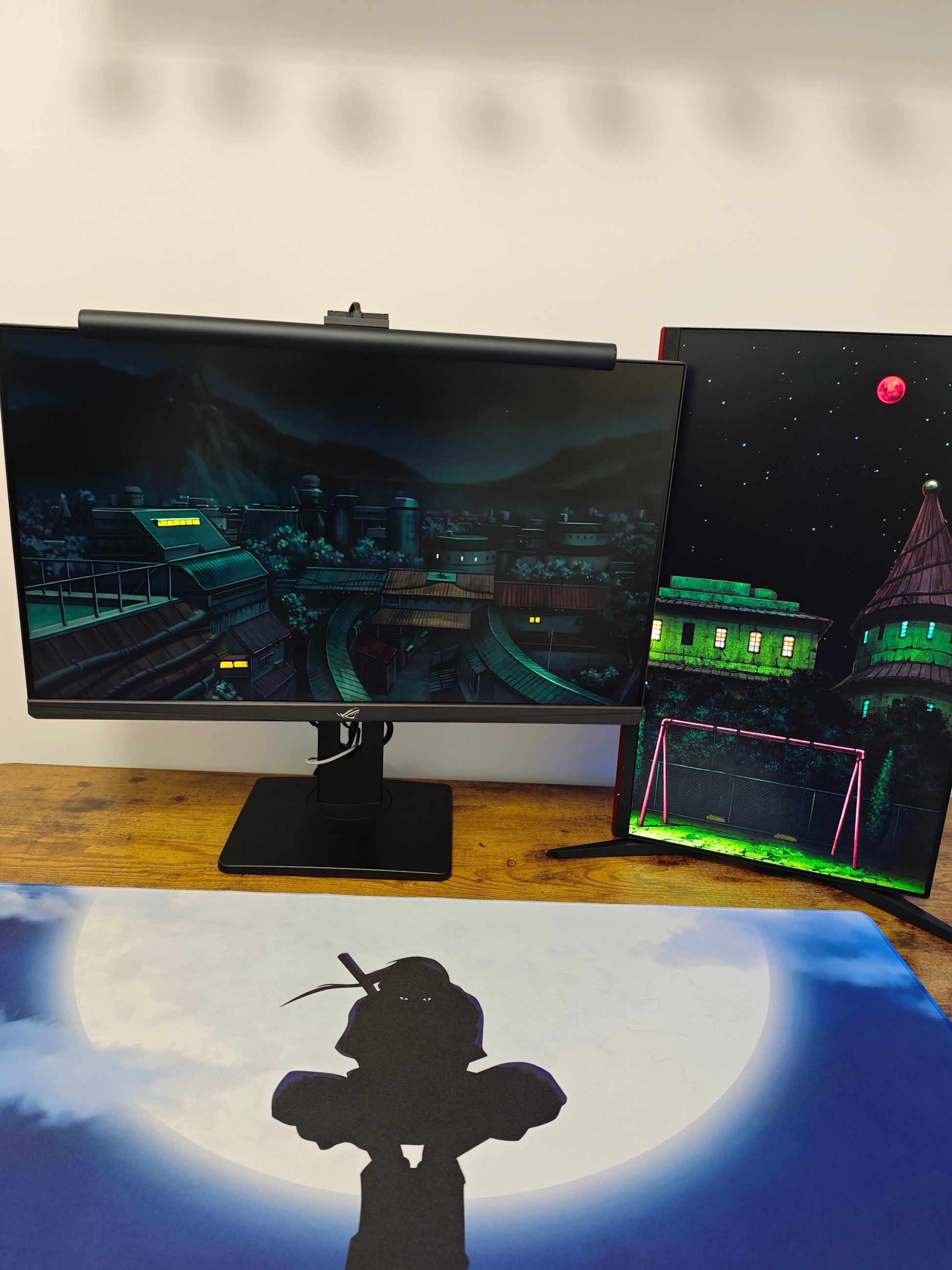 Mousepad Naruto cu personajul Itachi de mari dimensiuni pe birou în setup de gaming cu 2 monitoare.